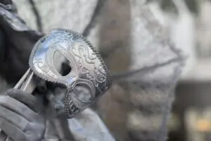 A silver mask is sitting on top of some leaves.